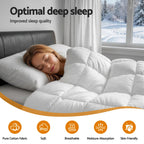 Woman sleeping under a white comforter with a snowy landscape outside the window.