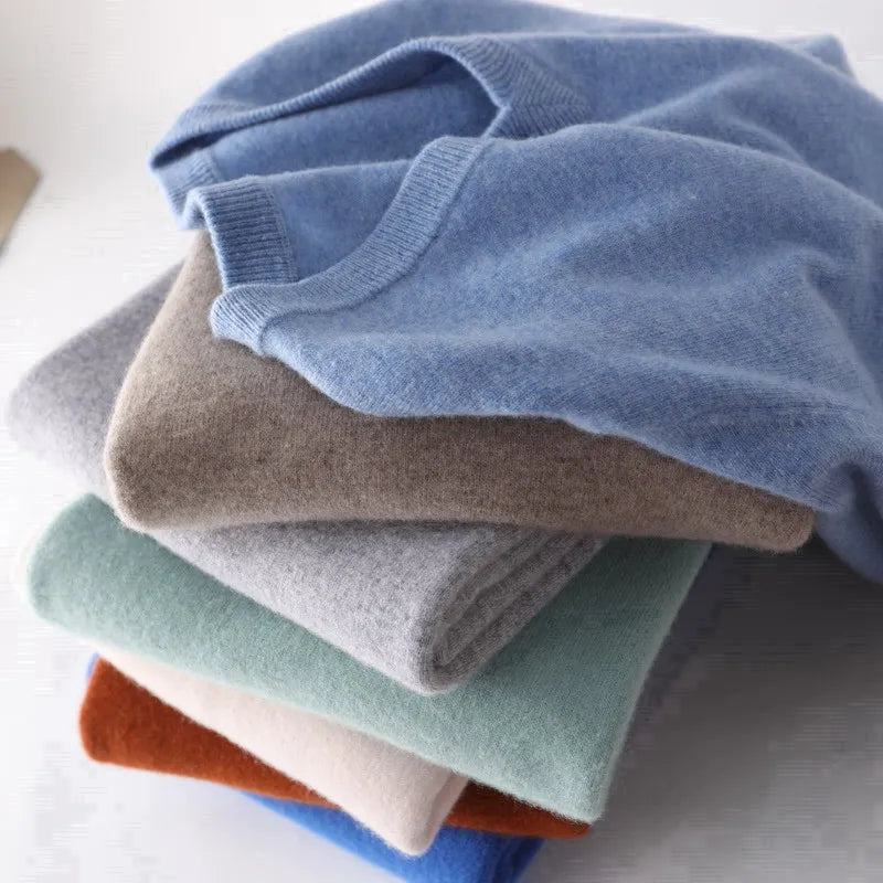 Stack of folded sweaters in various colors on a light background