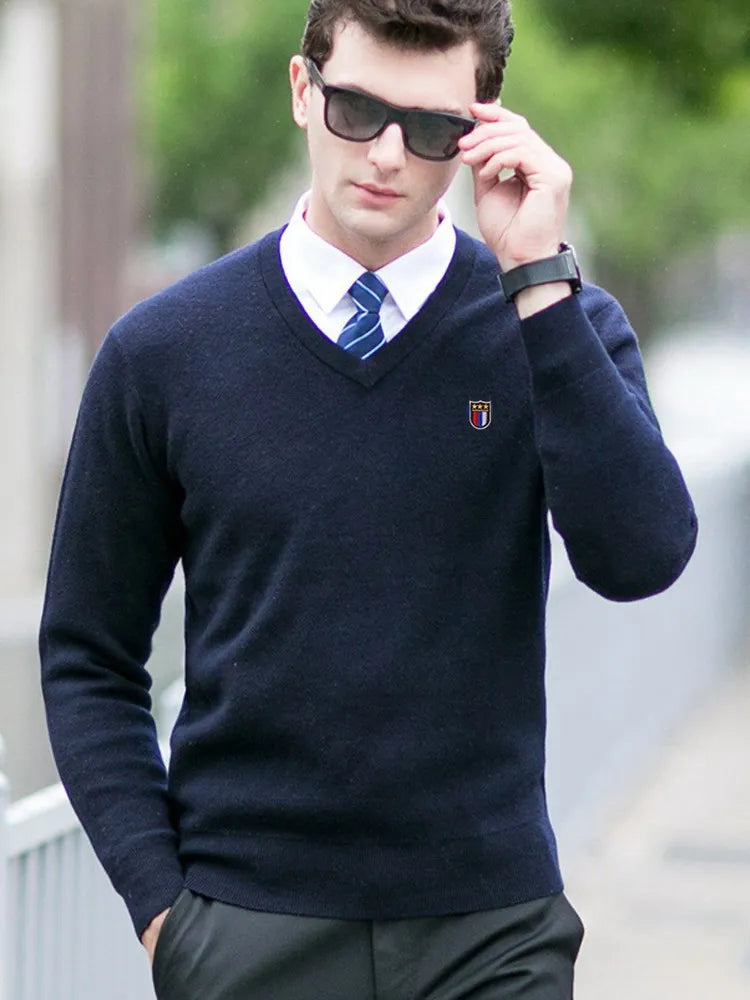 Man wearing a navy sweater with a logo, white shirt, and blue tie outdoors.