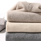 Stack of folded sweaters in beige, gray, and cream on a white surface