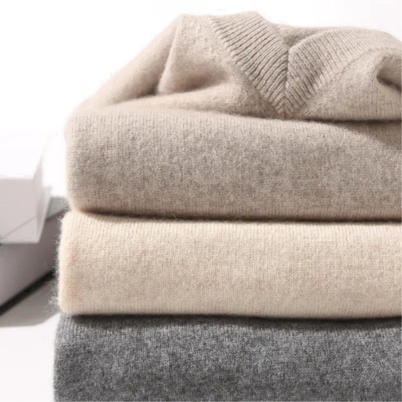 Stack of folded sweaters in beige, gray, and cream on a white surface
