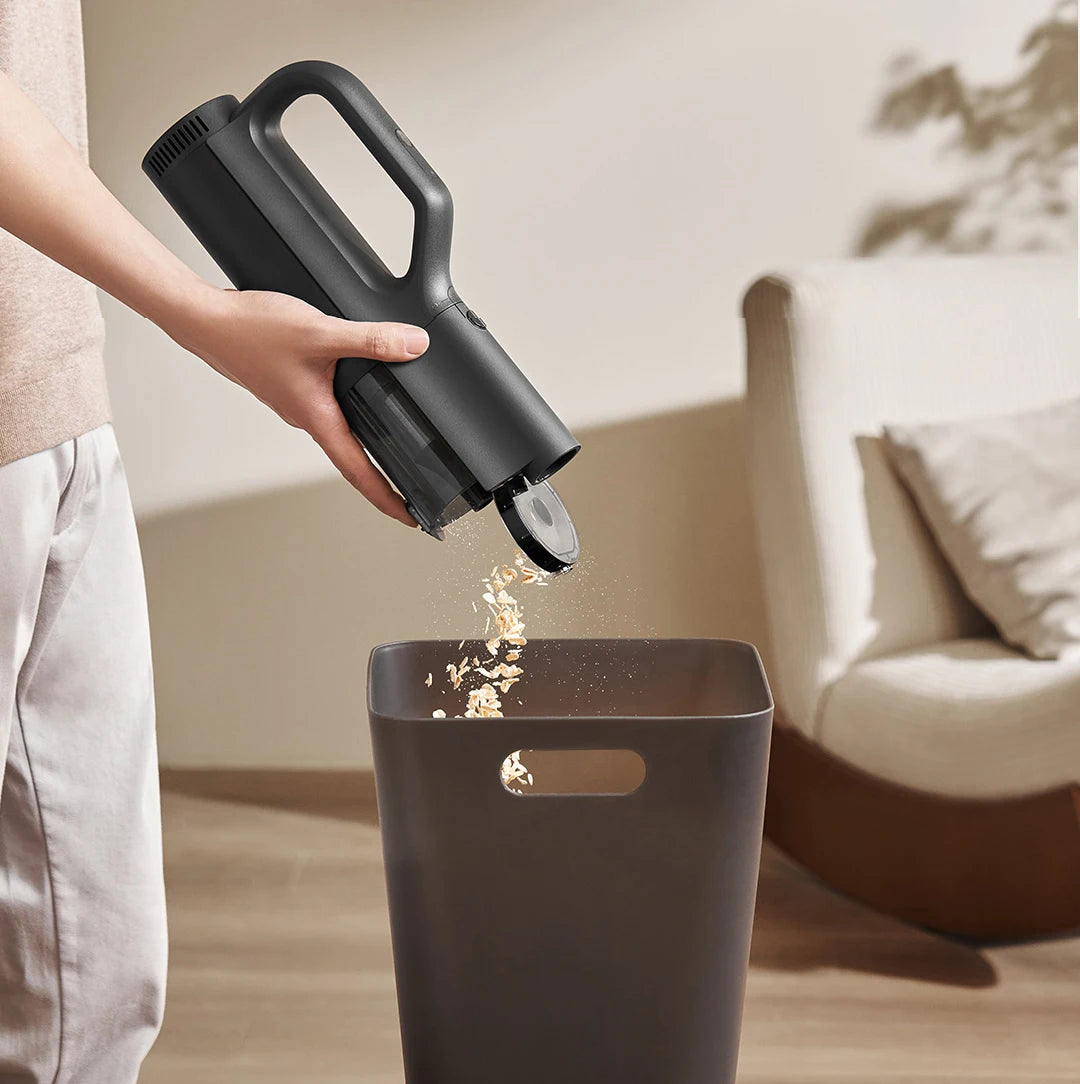 Person using a handheld vacuum cleaner to clean a trash can indoors.