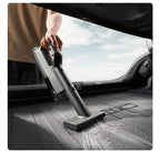 Person using a handheld vacuum cleaner inside a car with a clear sky visible through the window.