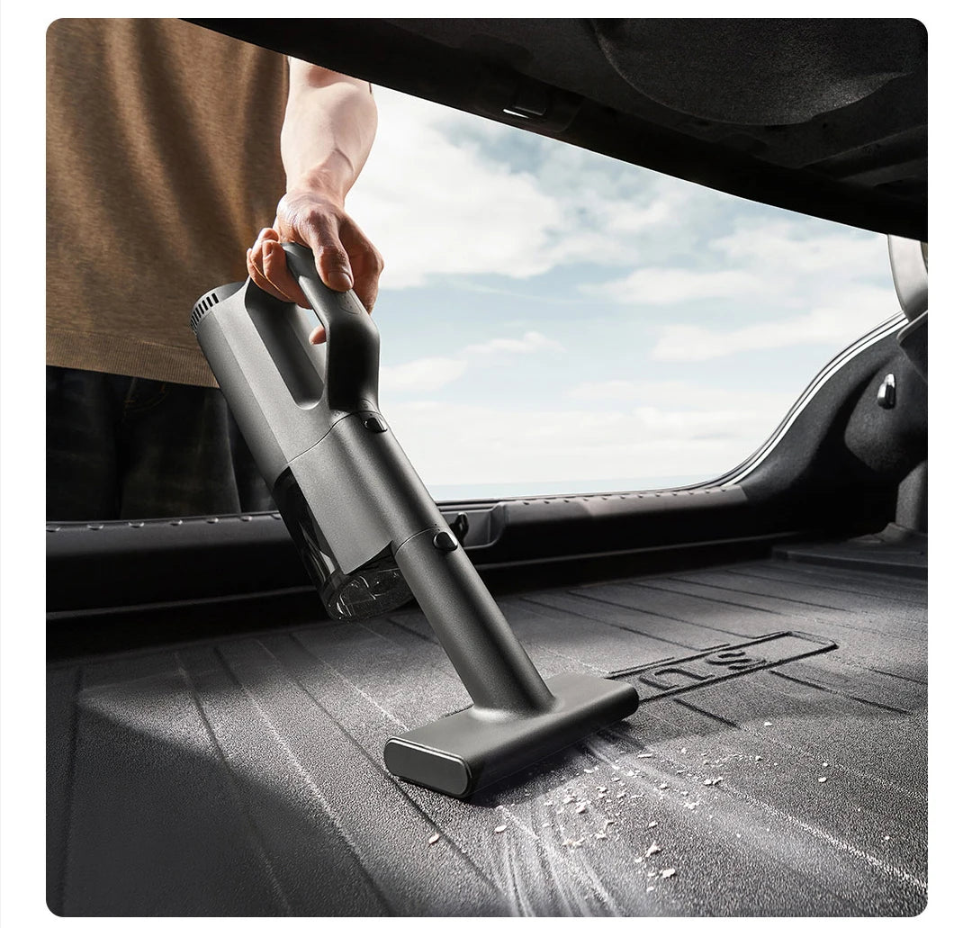Person using a handheld vacuum cleaner inside a car with a clear sky visible through the window.