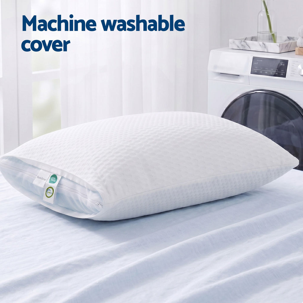 White pillow with machine washable cover on a bed next to a washing machine.